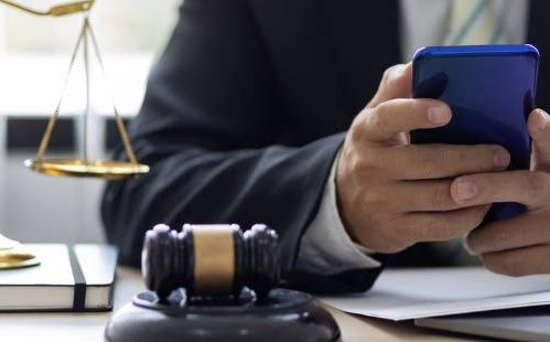 Profissional do Direito usa celular ao lado de martelo judicial